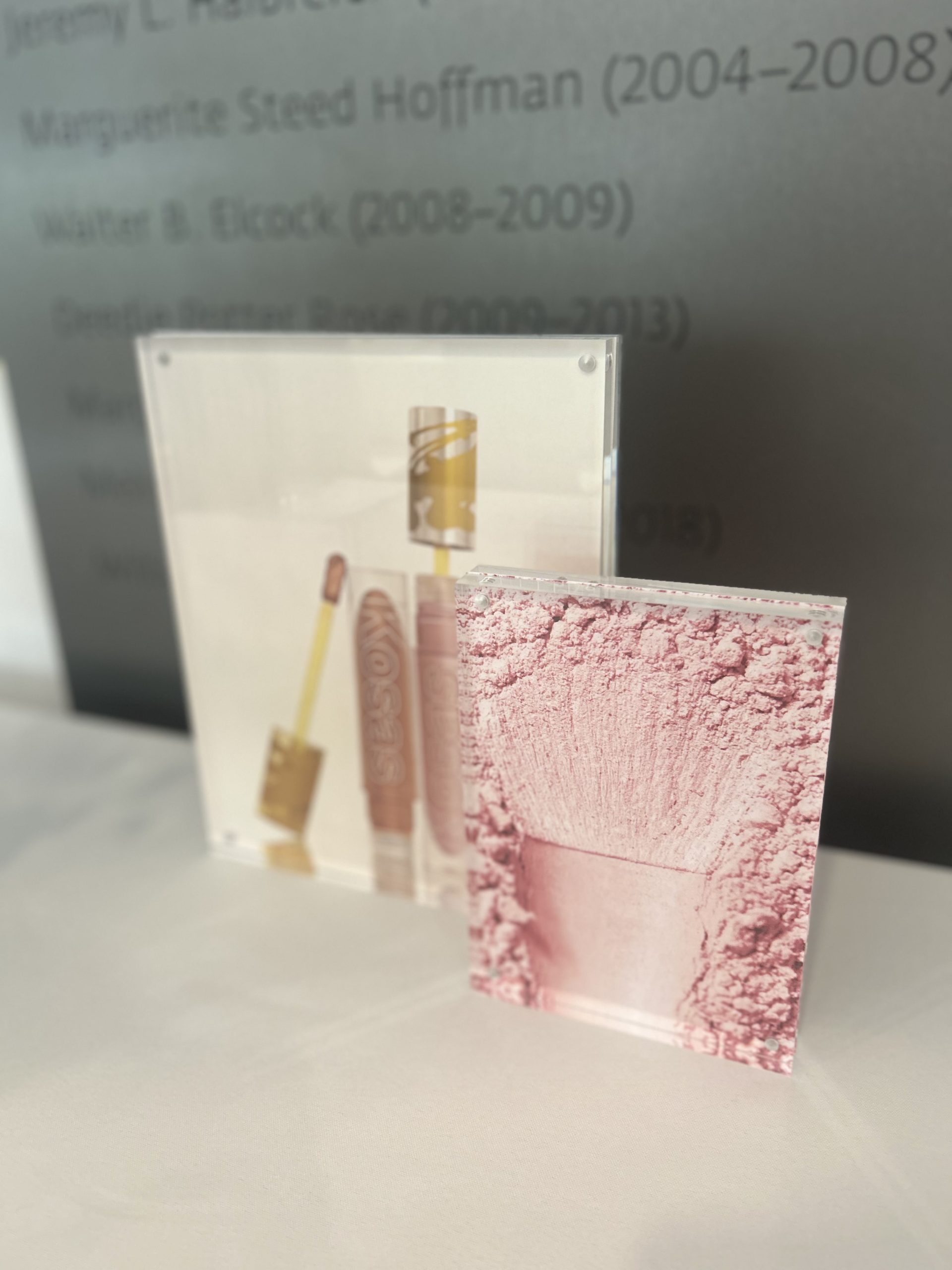 Kosas lip product and pink powder campaign imagery displayed in clear tabletop holders.