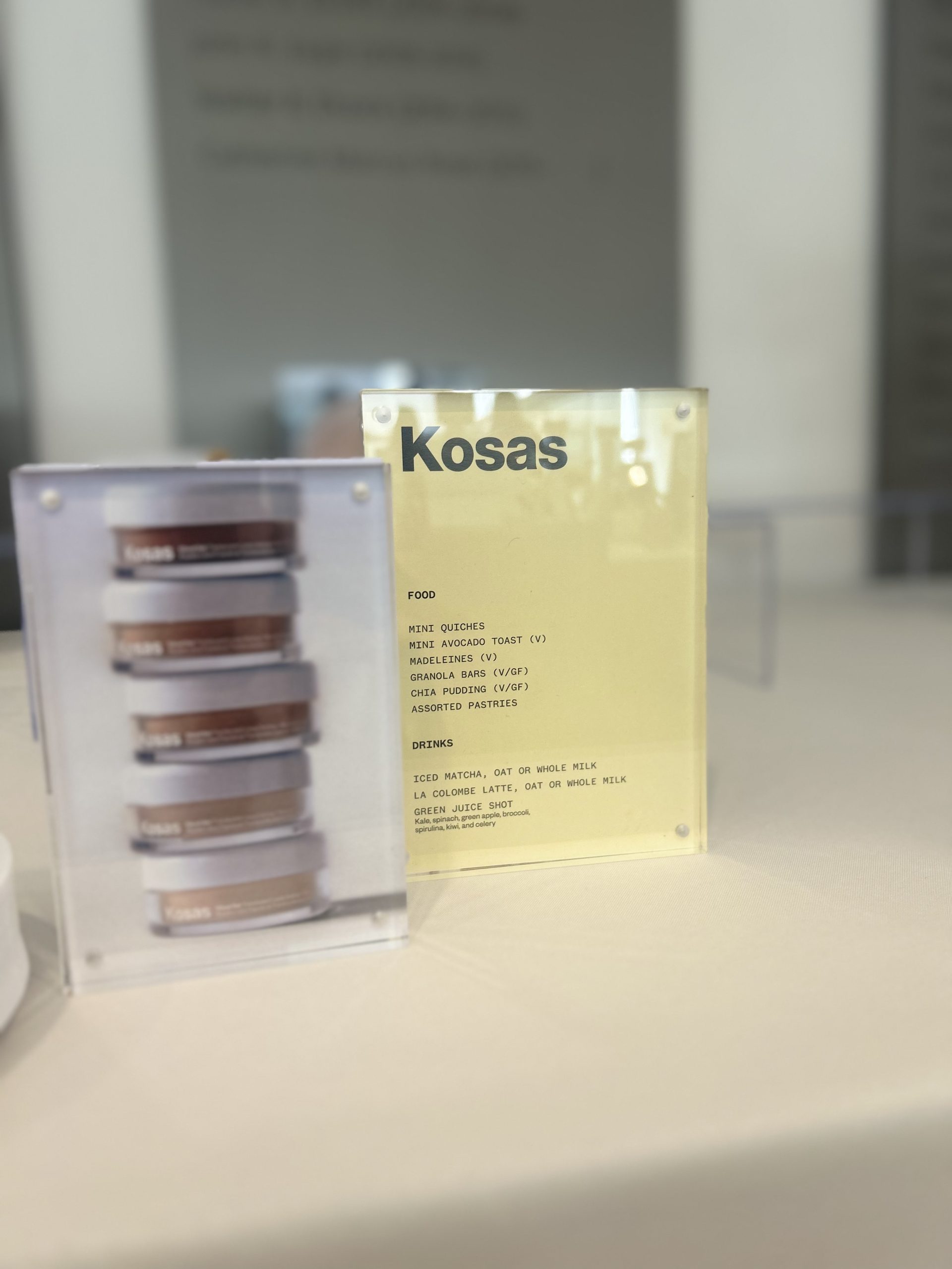 Kosas food and beverage menu displayed beside a cosmetics campaign card in clear holders.