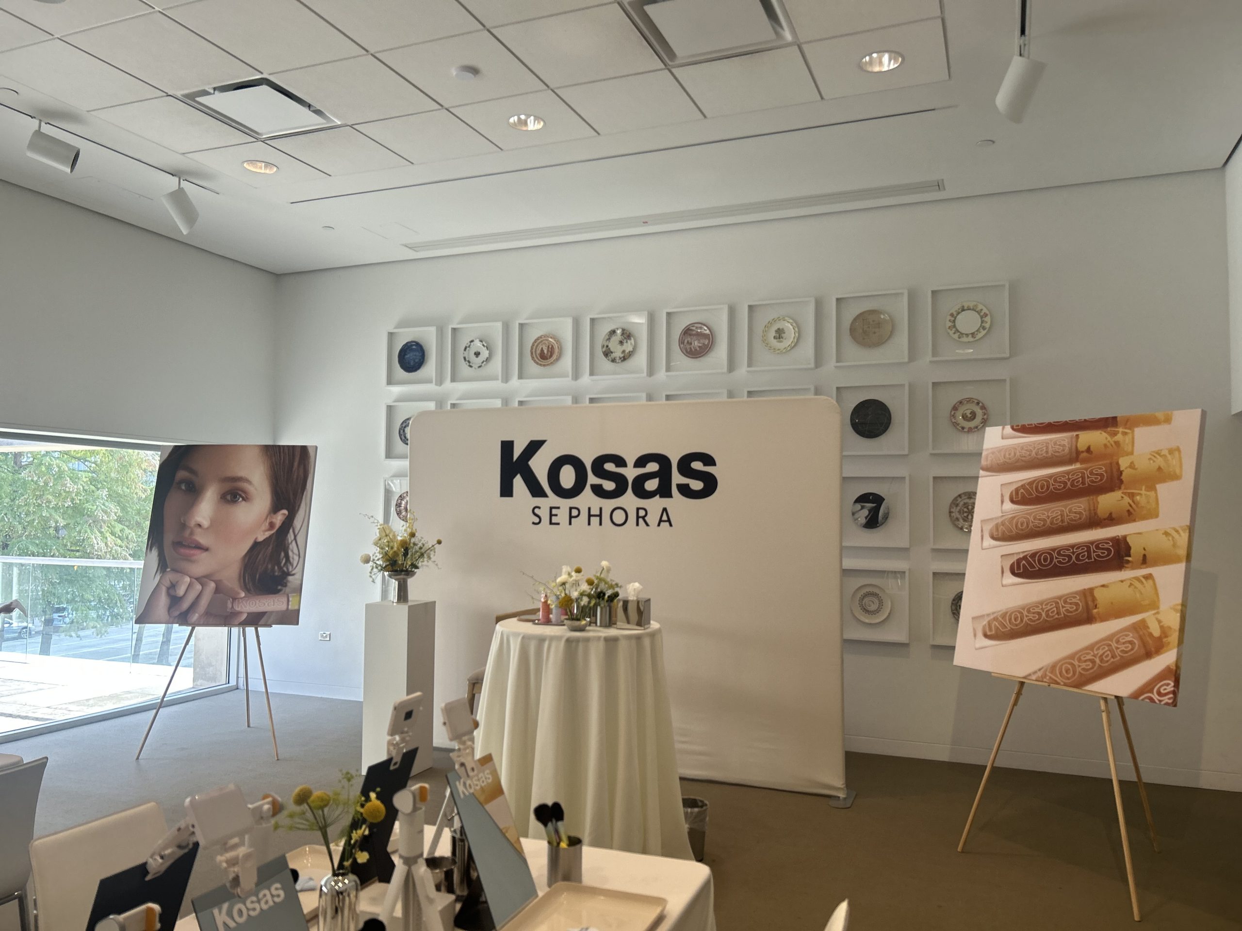 Kosas and Sephora logos on a cream fabric backdrop between two canvas campaign displays.