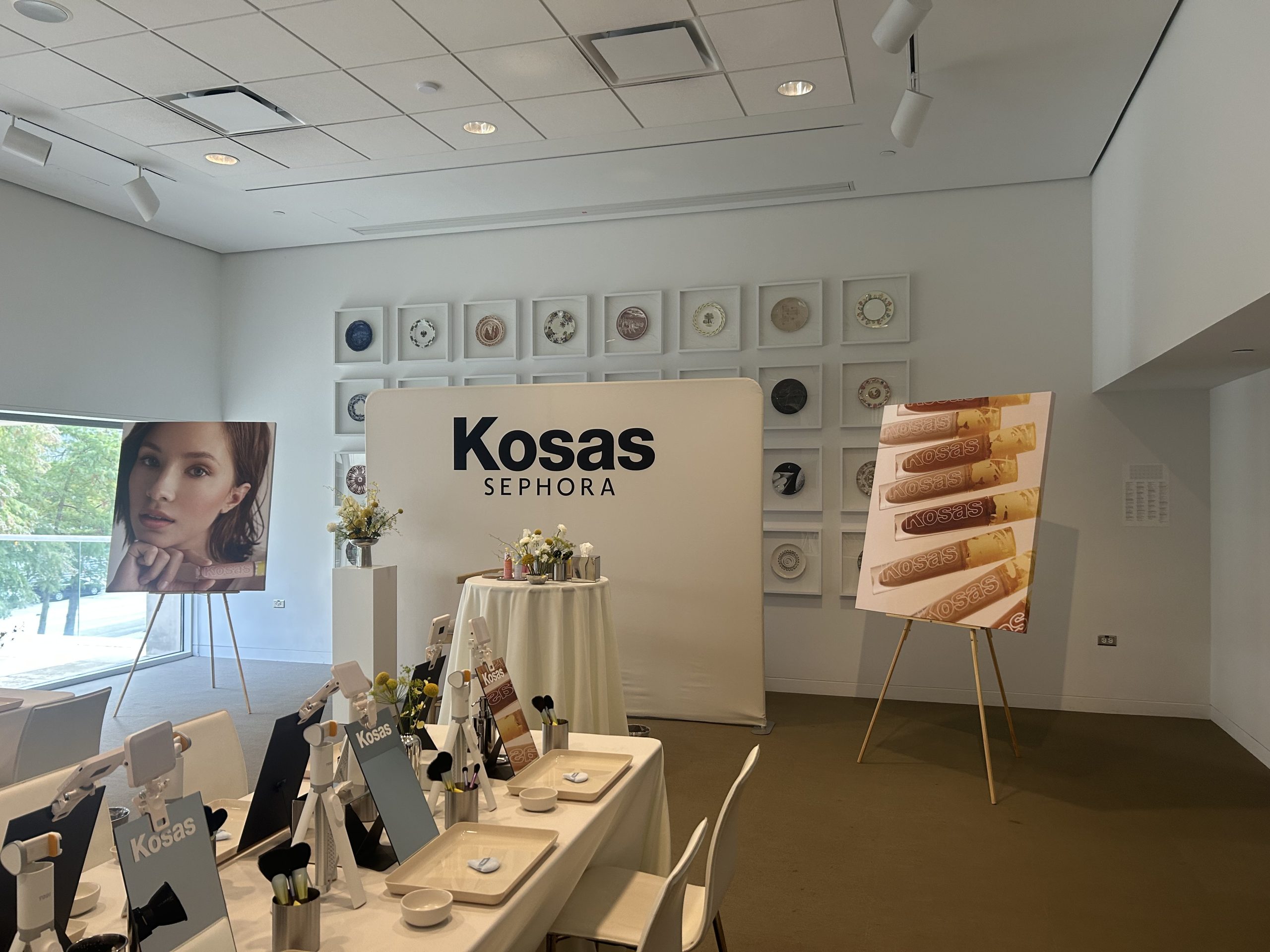 Kosas masterclass setup with a branded fabric backdrop, canvas displays, and rows of makeup mirrors.